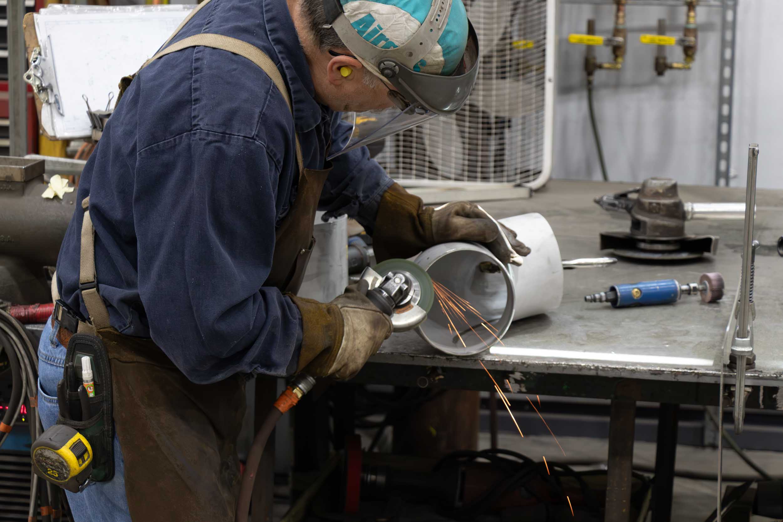 Worker grinding metal pipe in workshop